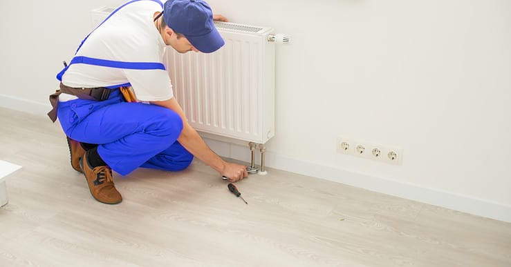 Un plombier installant un radiateur de chauffage avec sa clé à molette