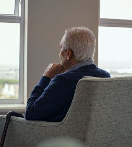 Un homme âgé assis sur un fauteuil et regardant par la fenêtre