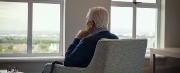 Un homme âgé assis sur un fauteuil et regardant par la fenêtre