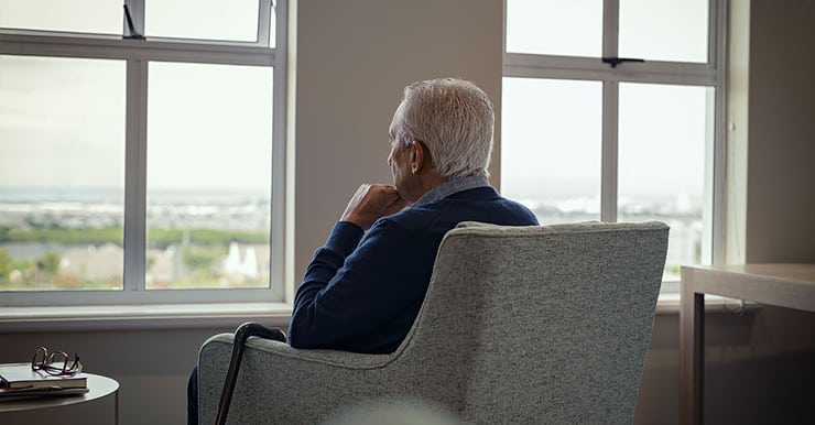 Un homme âgé assis sur un fauteuil et regardant par la fenêtre
