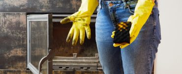 Une jeune femme en jeans et des gants jaunes nettoyant la cheminée