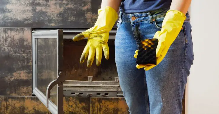 Une jeune femme en jeans et des gants jaunes nettoyant la cheminée