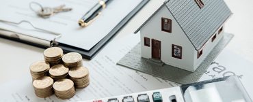 Illustation d'un prêt immobilier avec une maquette de maison, des pièces, une calculatrice et un contrat sur la table