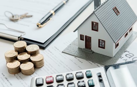 Illustation d'un prêt immobilier avec une maquette de maison, des pièces, une calculatrice et un contrat sur la table