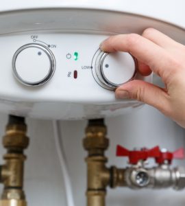 Main d'une femme réglant le thermostat du chauffe-eau électrique sur le niveau minimum