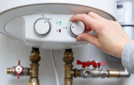 Main d'une femme réglant le thermostat du chauffe-eau électrique sur le niveau minimum
