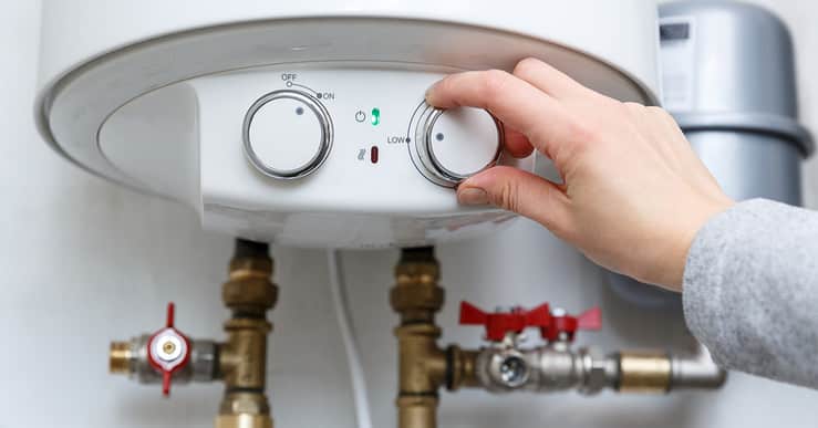 Main d'une femme réglant le thermostat du chauffe-eau électrique sur le niveau minimum