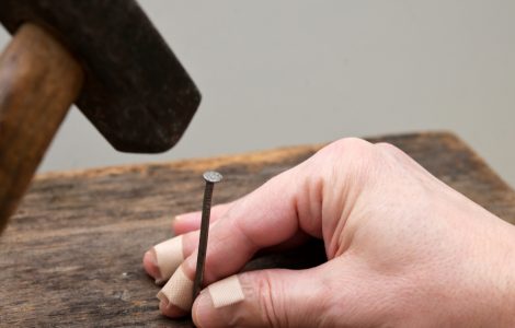 Une main avec du sparadrap sur les doigts essaie de planter un clou