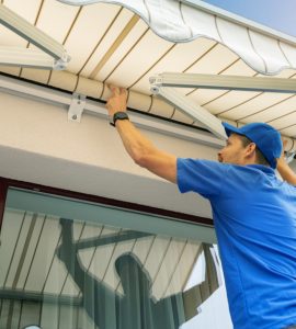 Un homme en casquette bleue installe un store banne sur la terrasse