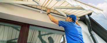 Un homme en casquette bleue installe un store banne sur la terrasse