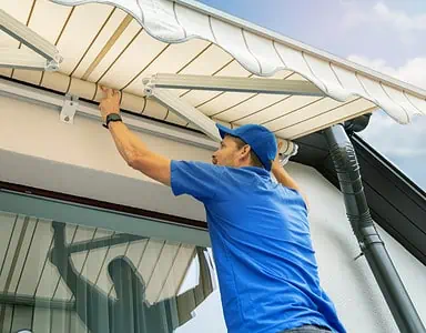 Un homme en casquette bleue installe un store banne sur la terrasse