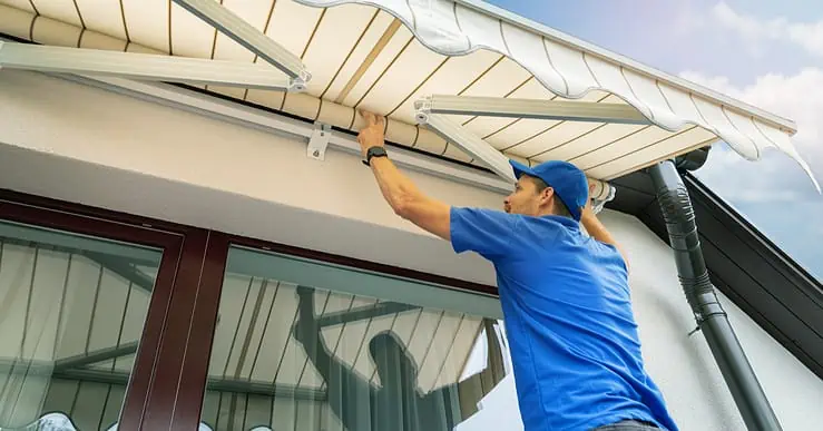 Un homme en casquette bleue installe un store banne sur la terrasse