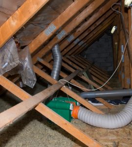 Des gaines grises passent dans la sous-toiture en bois d'une maison
