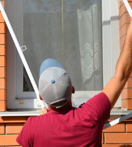 Un homme en casquette installe une moustiquaire sur une fenêtre