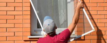 Un homme en casquette installe une moustiquaire sur une fenêtre