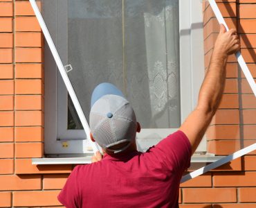 Un homme en casquette installe une moustiquaire sur une fenêtre