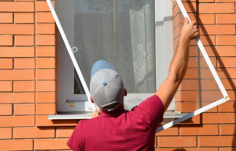 Un homme en casquette installe une moustiquaire sur une fenêtre