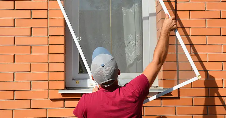 Un homme en casquette installe une moustiquaire sur une fenêtre