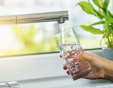 Zoom sur la main d'une femme en train de remplir un verre d'eau du robinet