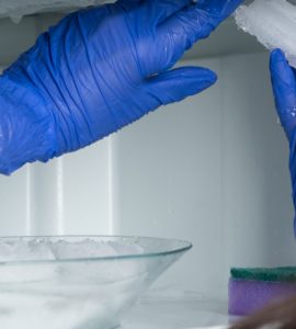 Une femme aux gants bleus enlève la glace de son réfrigérateur