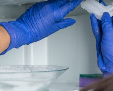 Une femme aux gants bleus enlève la glace de son réfrigérateur