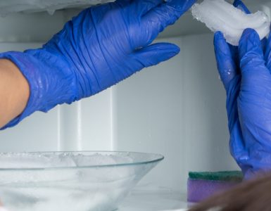 Une femme aux gants bleus enlève la glace de son réfrigérateur