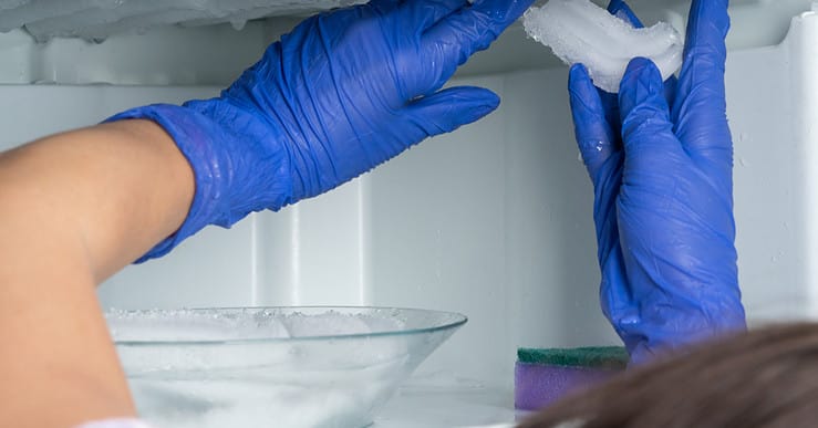 Une femme aux gants bleus enlève la glace de son réfrigérateur