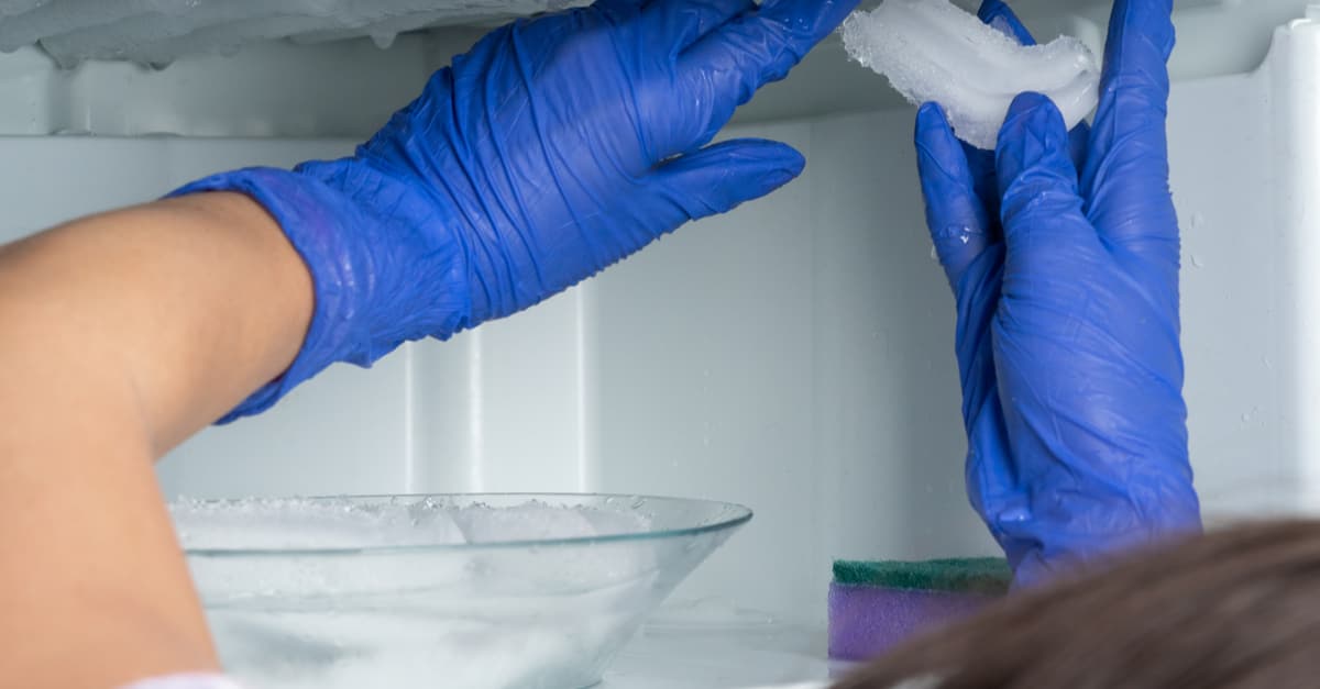 Une femme aux gants bleus enlève la glace de son réfrigérateur