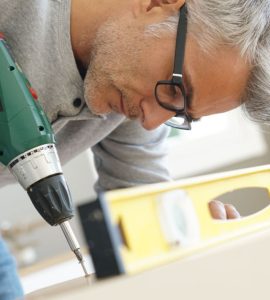 Un homme à lunette en train d’assembler un meuble à l’aide de sa visseuse électrique