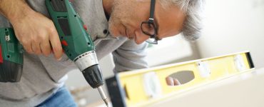 Un homme à lunette en train d’assembler un meuble à l’aide de sa visseuse électrique