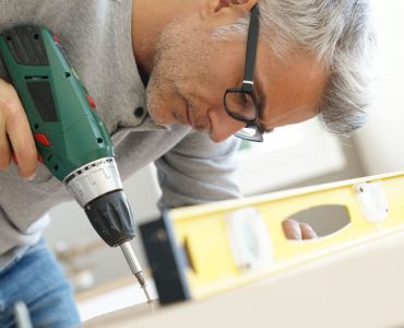 Un homme à lunette en train d’assembler un meuble à l’aide de sa visseuse électrique