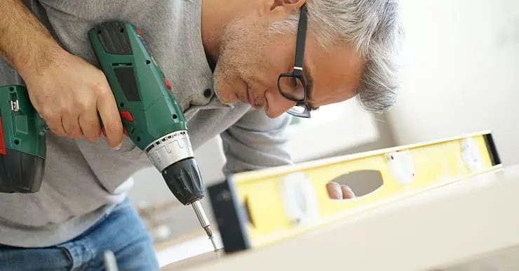 Un homme à lunette en train d’assembler un meuble à l’aide de sa visseuse électrique