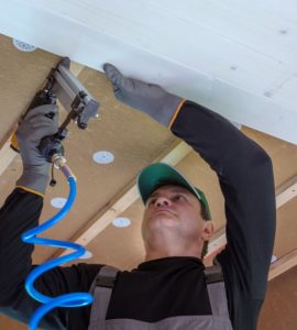 Un homme en casquette installe un panneau en bois blanc sur le plafond