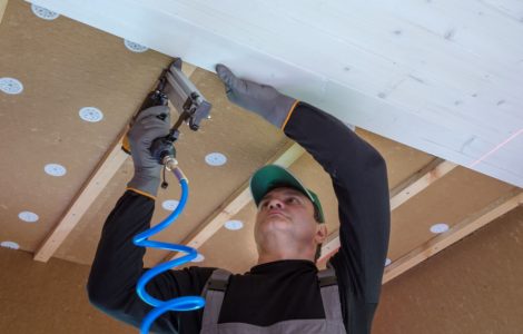 Un homme en casquette installe un panneau en bois blanc sur le plafond