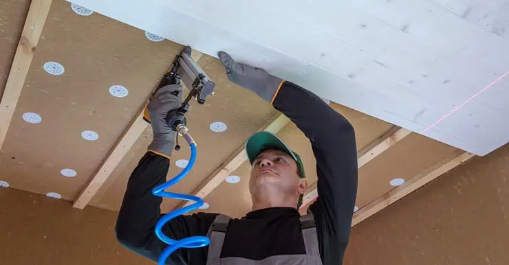 Un homme en casquette installe un panneau en bois blanc sur le plafond