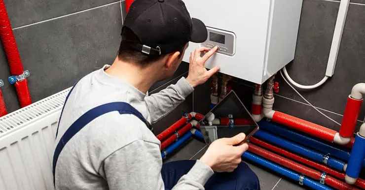 Un homme en combinaison de travail et avec une tablette à la main vérifie le système de chauffage