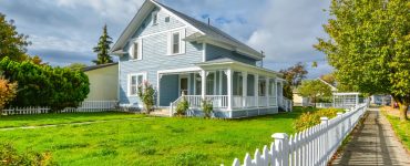 Une grande maison bleue avec un grand jardin et une palissade blanche