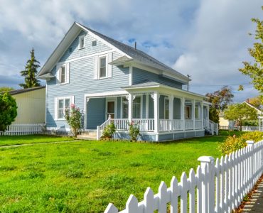 Une grande maison bleue avec un grand jardin et une palissade blanche