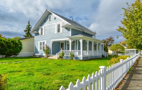 Une grande maison bleue avec un grand jardin et une palissade blanche