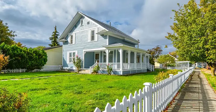 Une grande maison bleue avec un grand jardin et une palissade blanche