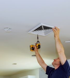 Un homme en train de visser un couvercle de ventilation d'air au plafond