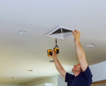 Un homme en train de visser un couvercle de ventilation d'air au plafond