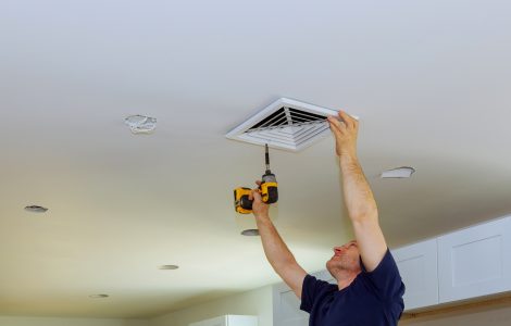 Un homme en train de visser un couvercle de ventilation d'air au plafond