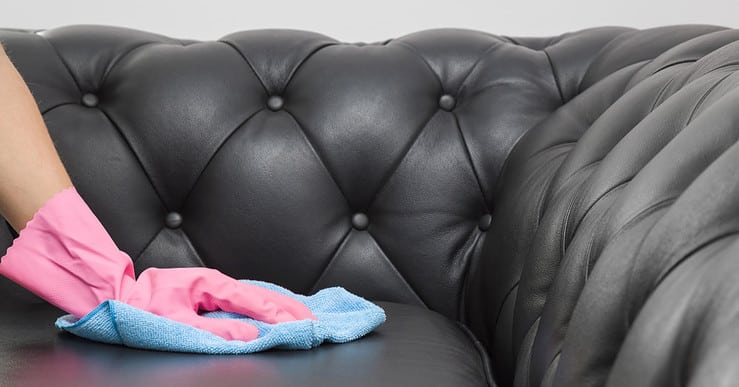 Main d'une femme nettoyant un canapé en cuir noir avec son chiffon bleu