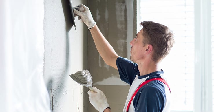 Un homme applique un cimentage sur le mur à l'aide de ces spatules