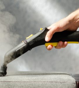 Une personne nettoie le canapé avec un nettoyeur à vapeur