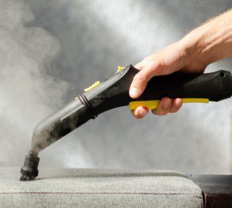 Une personne nettoie le canapé avec un nettoyeur à vapeur