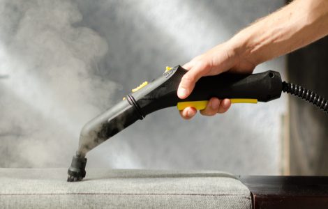 Une personne nettoie le canapé avec un nettoyeur à vapeur