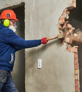 Un ouvrier abat un mur en briques avec son marteau