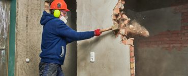 Un ouvrier abat un mur en briques avec son marteau